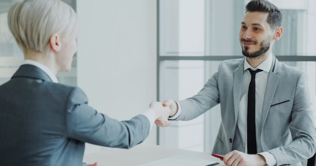 Two professionals shaking hands across a table after a successful tech job offer negotiation