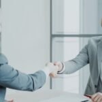 Two professionals shaking hands across a table after a successful tech job offer negotiation
