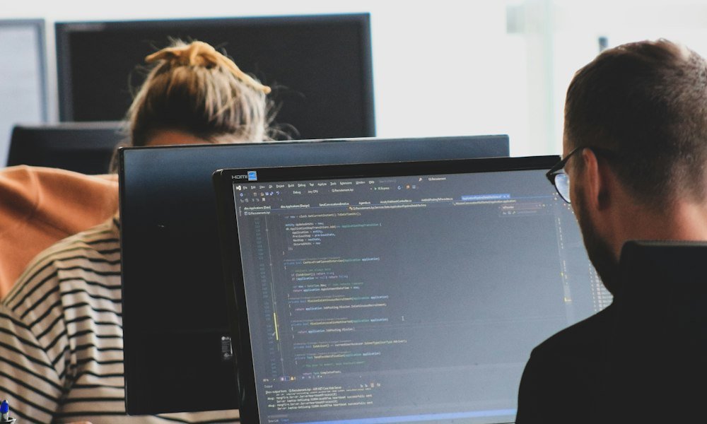 Two engineers reviewing code and architecture on monitors in a bright office